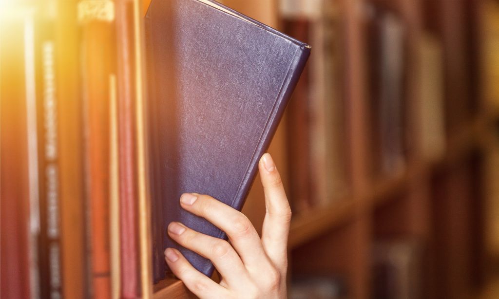 Hand holding book on a shelf