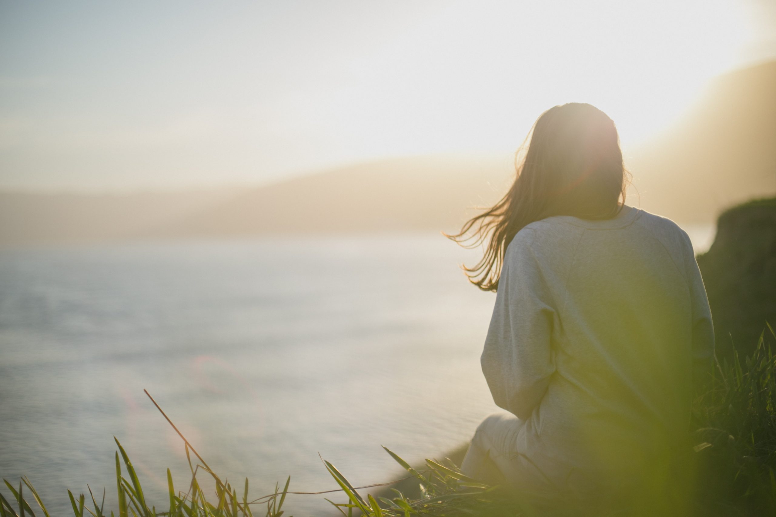 A woman sits by the shore and looks out at the sea.