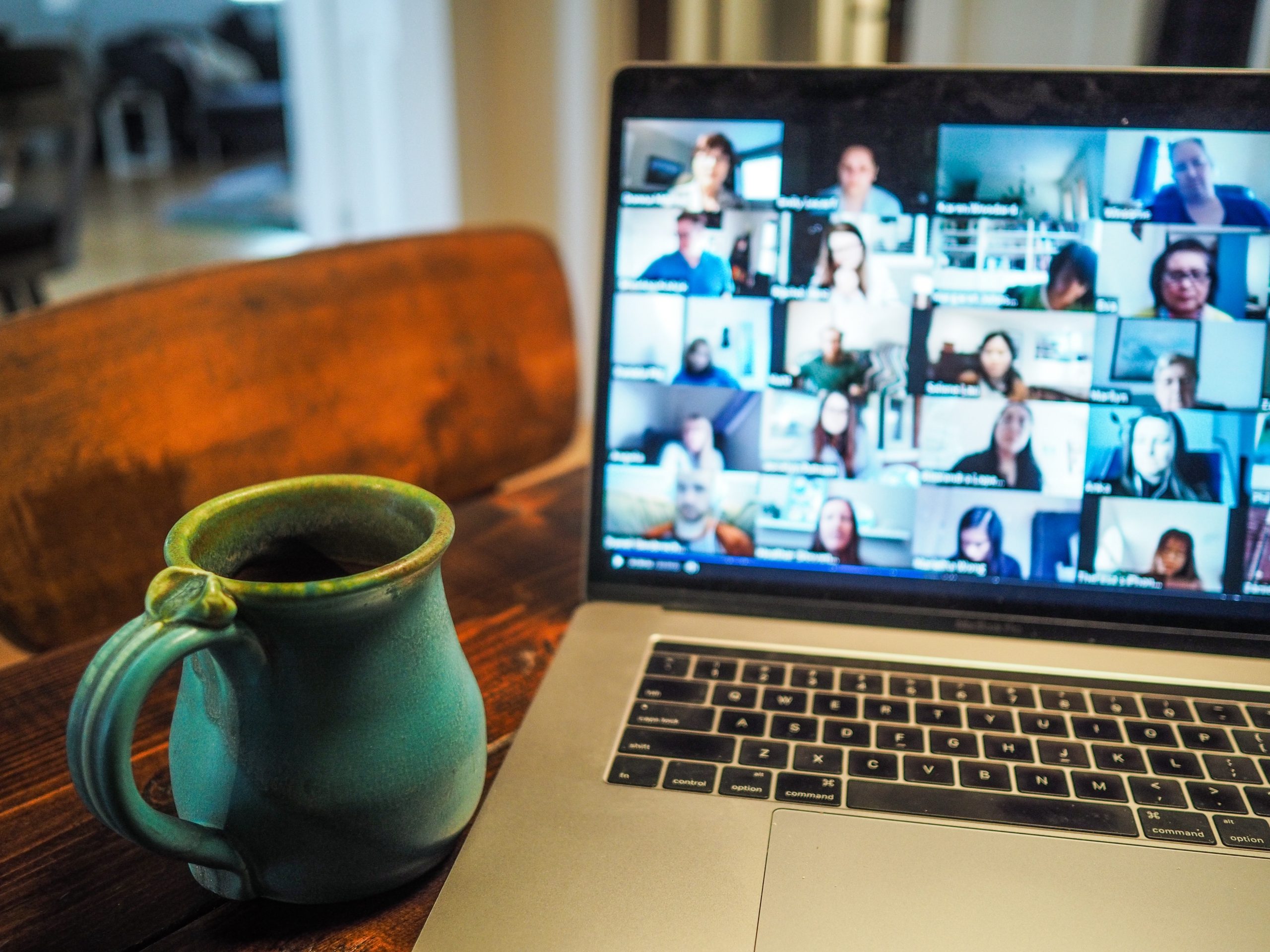 A coffee cup sits next to a laptop with many faces on a zoom chat.