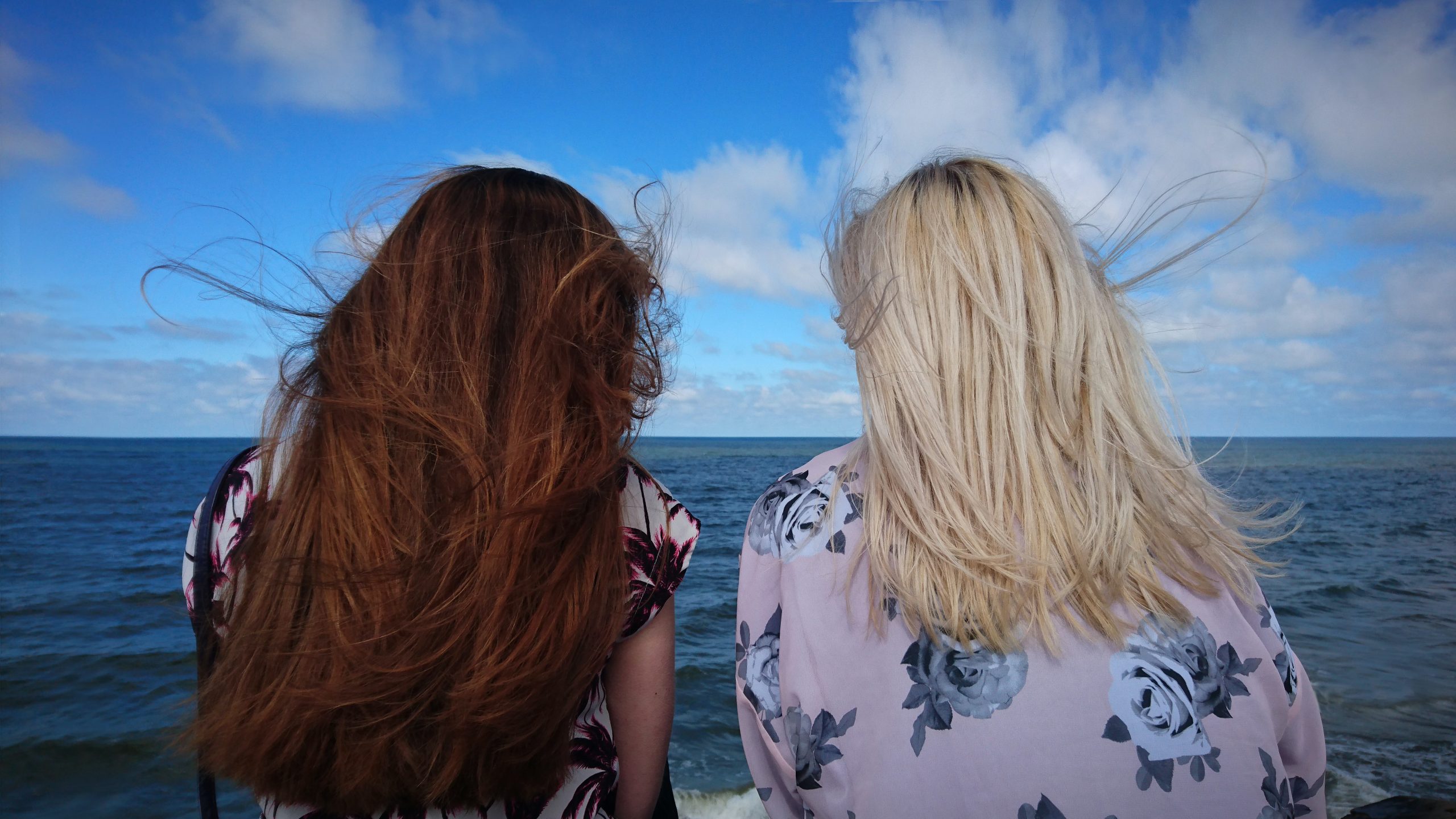 Two women sit close together and look out at the ocean.