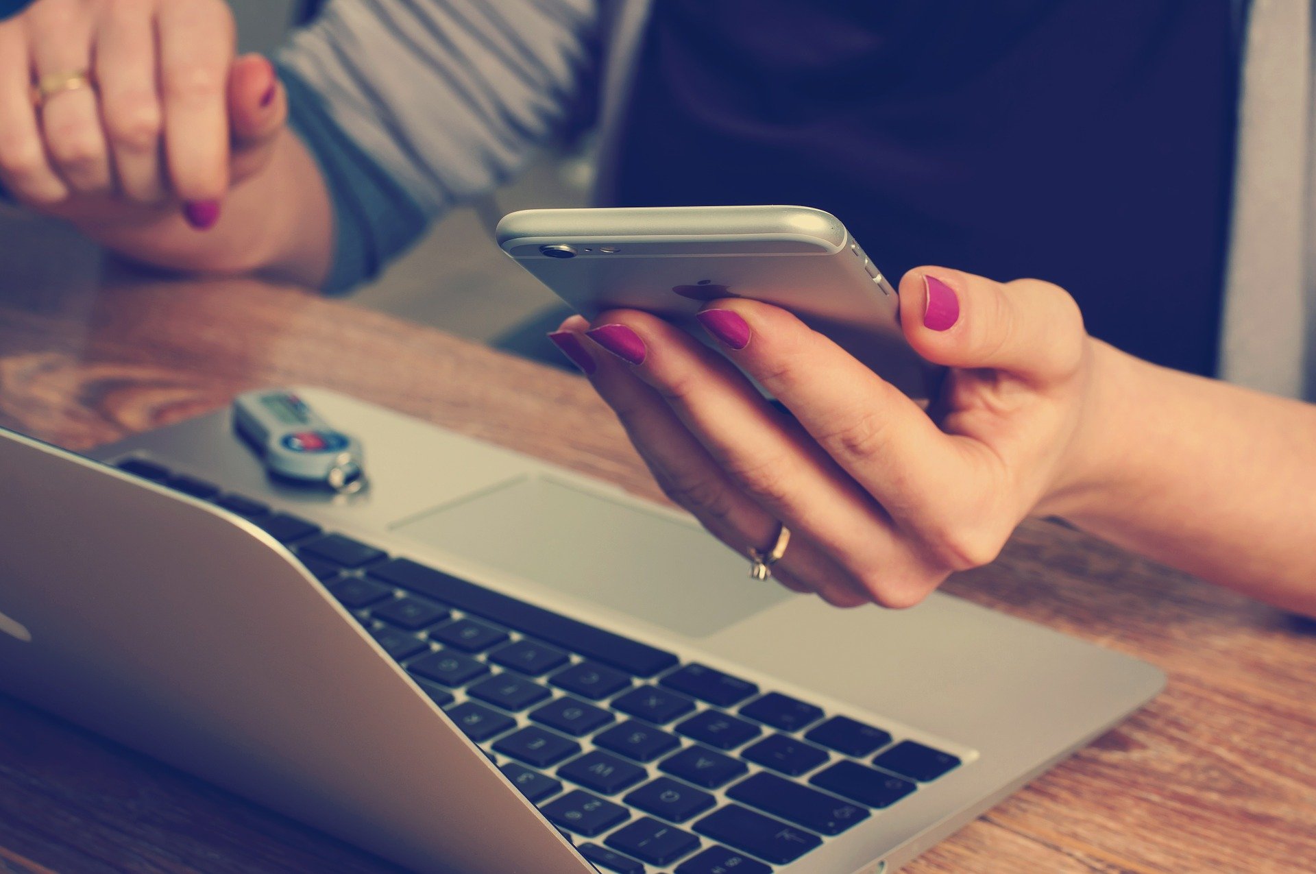 A woman holds a phone and sits at a computer desk.