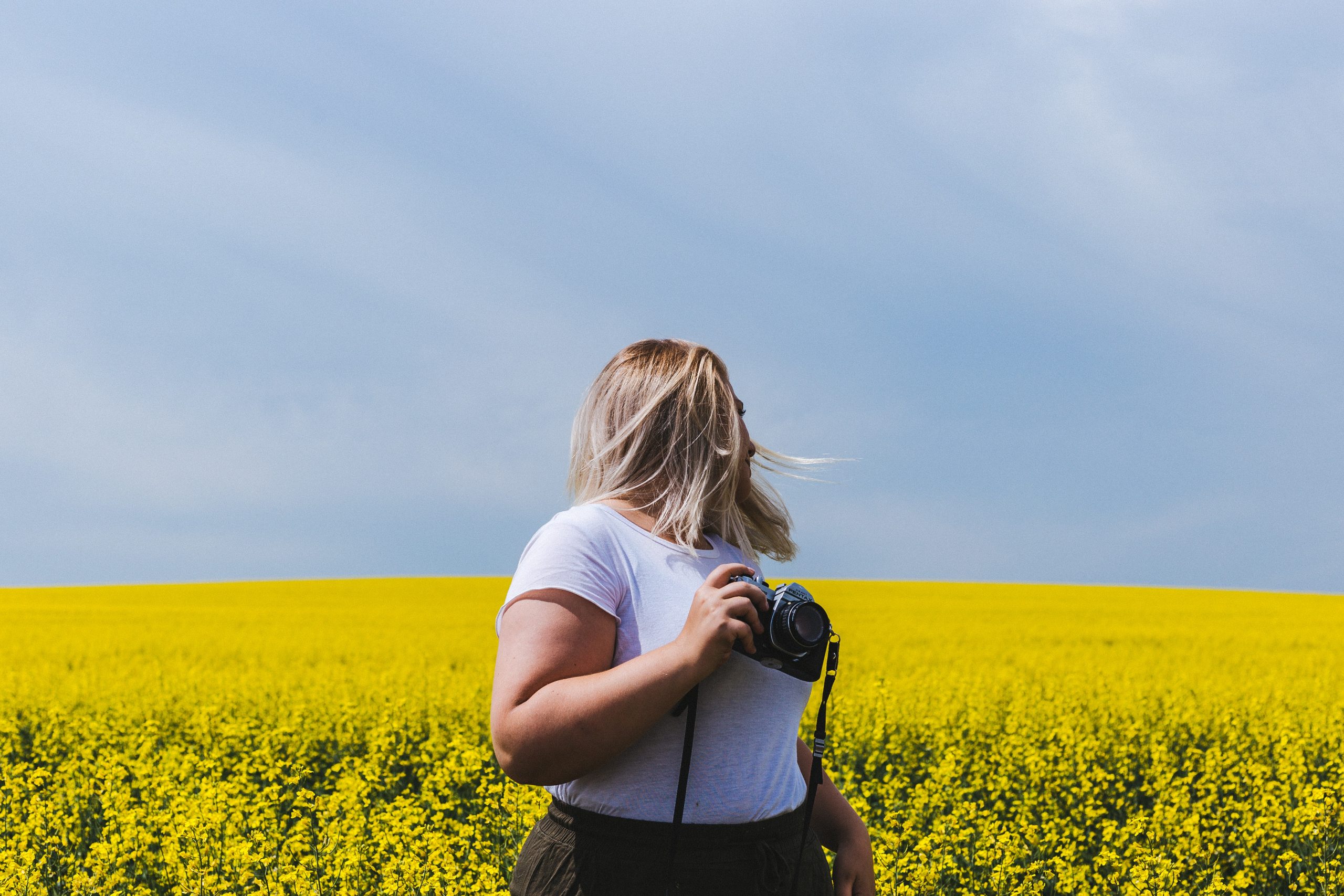 A large looks over her shoulder in the canola field and holds a camera.