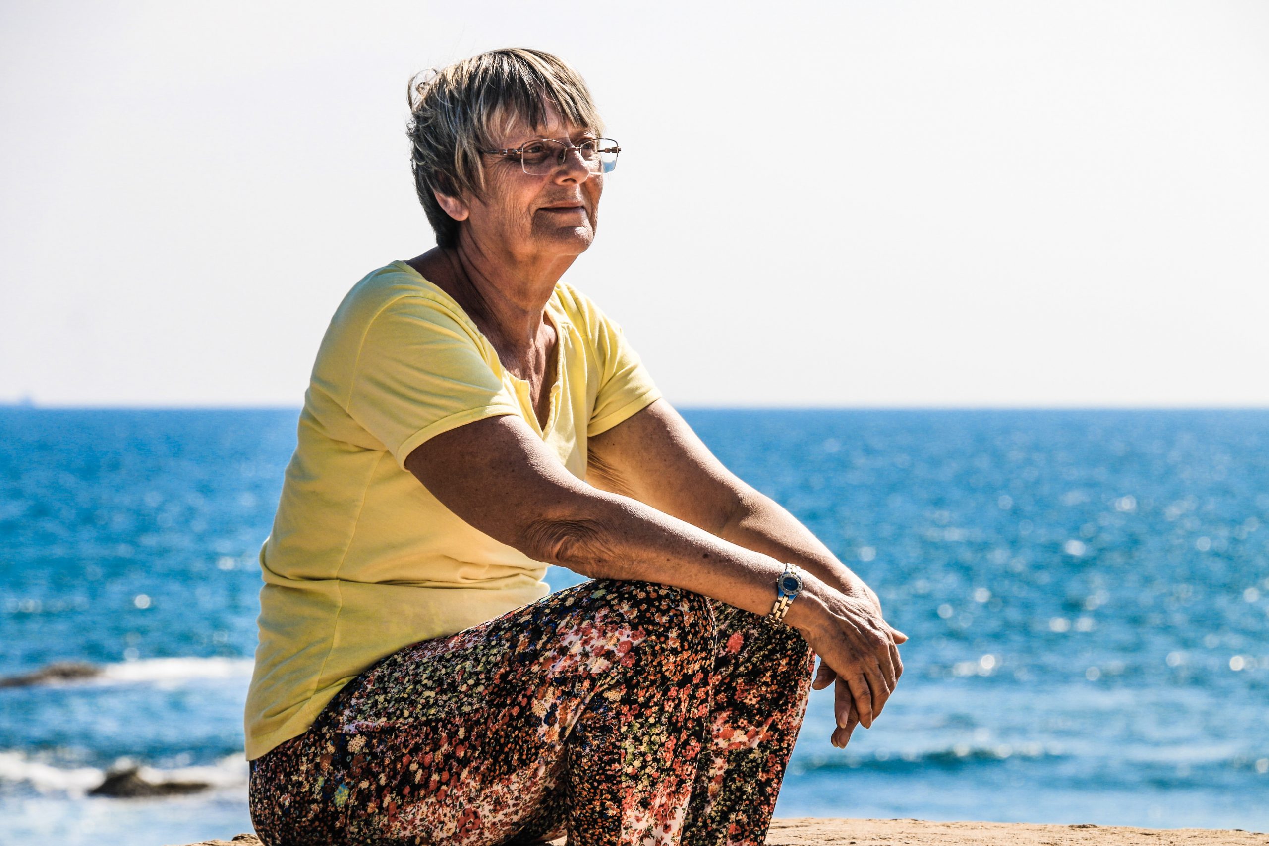 An older woman looks out at the sea and smiles.