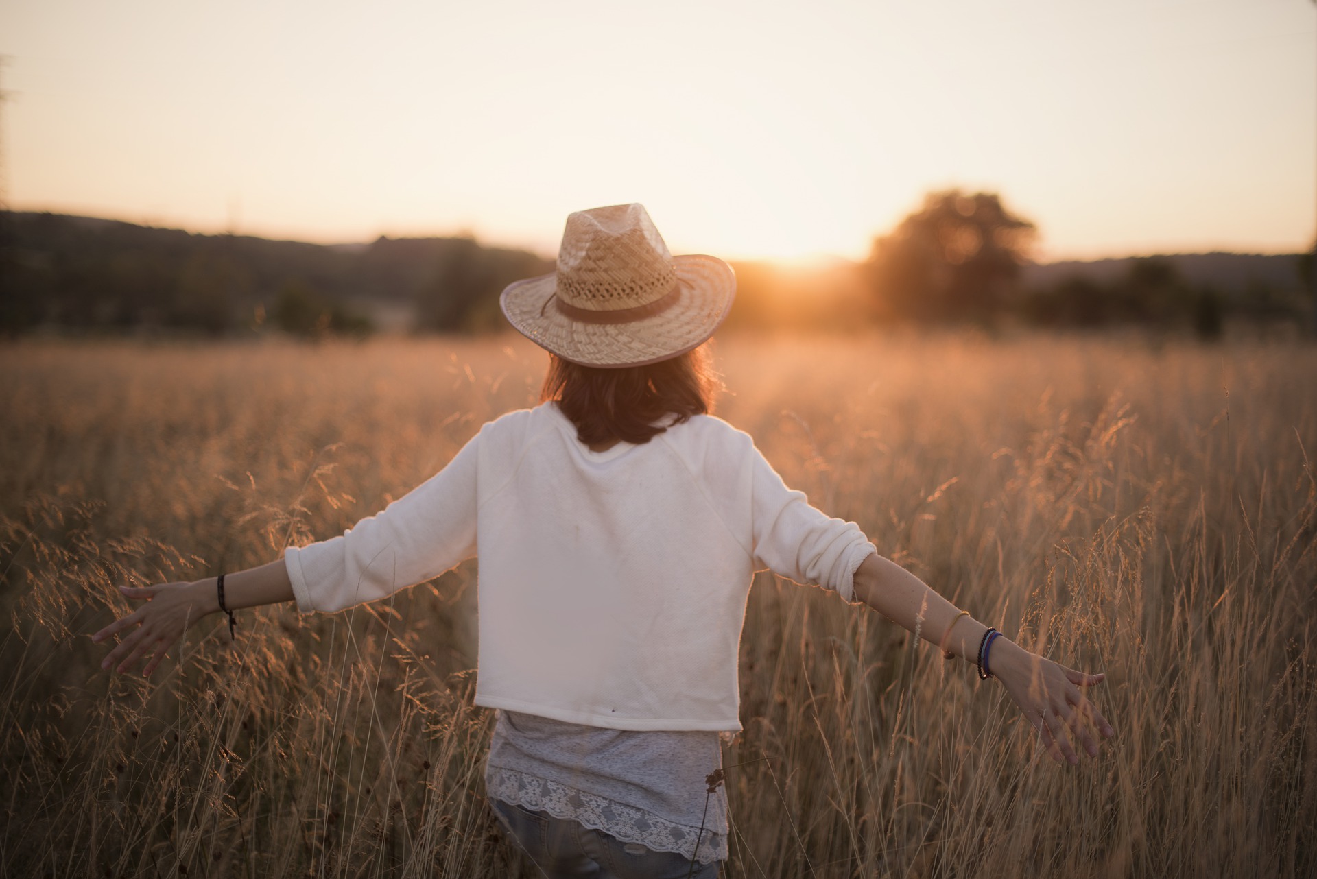 A woman stands facing the sunset with her arms out.