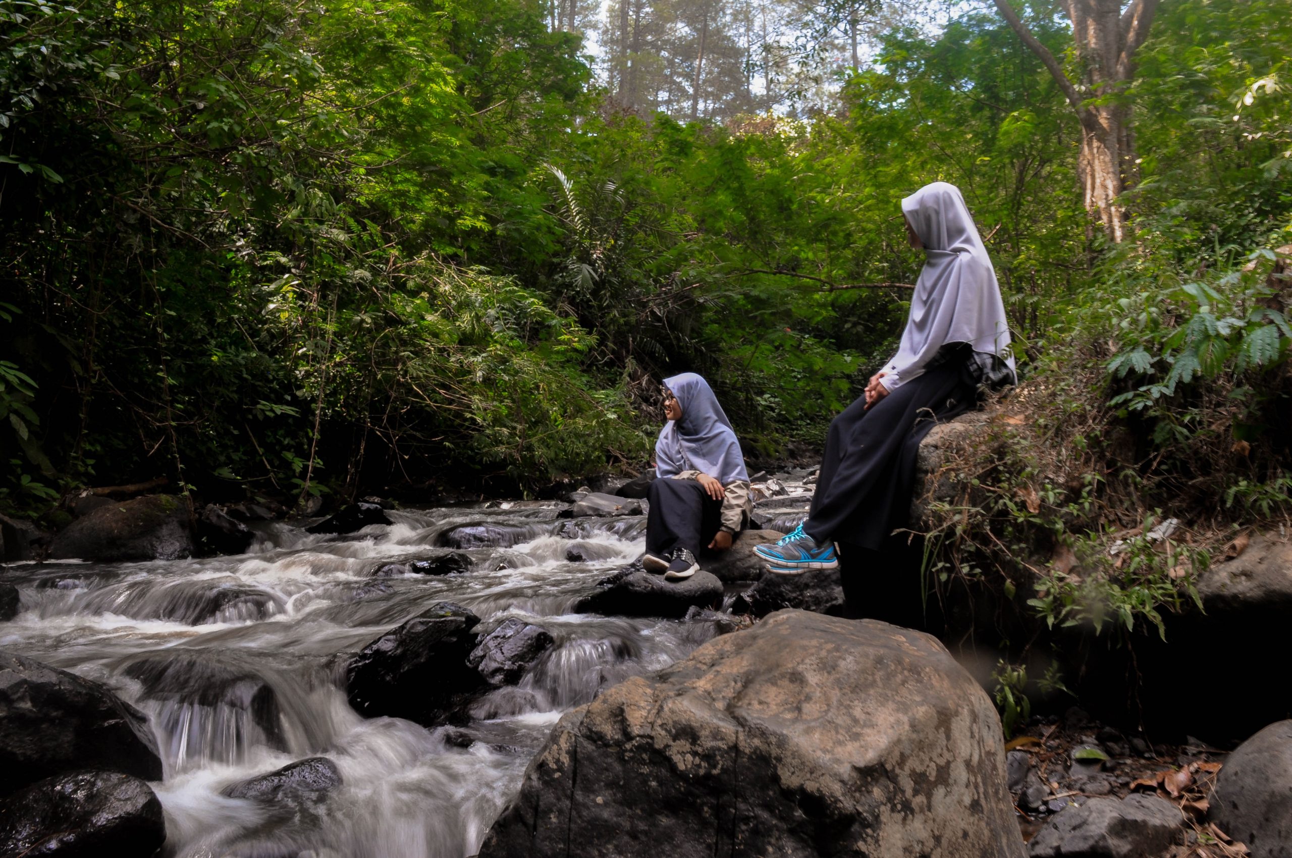 Two young women in hijabs sit by a waterfall.