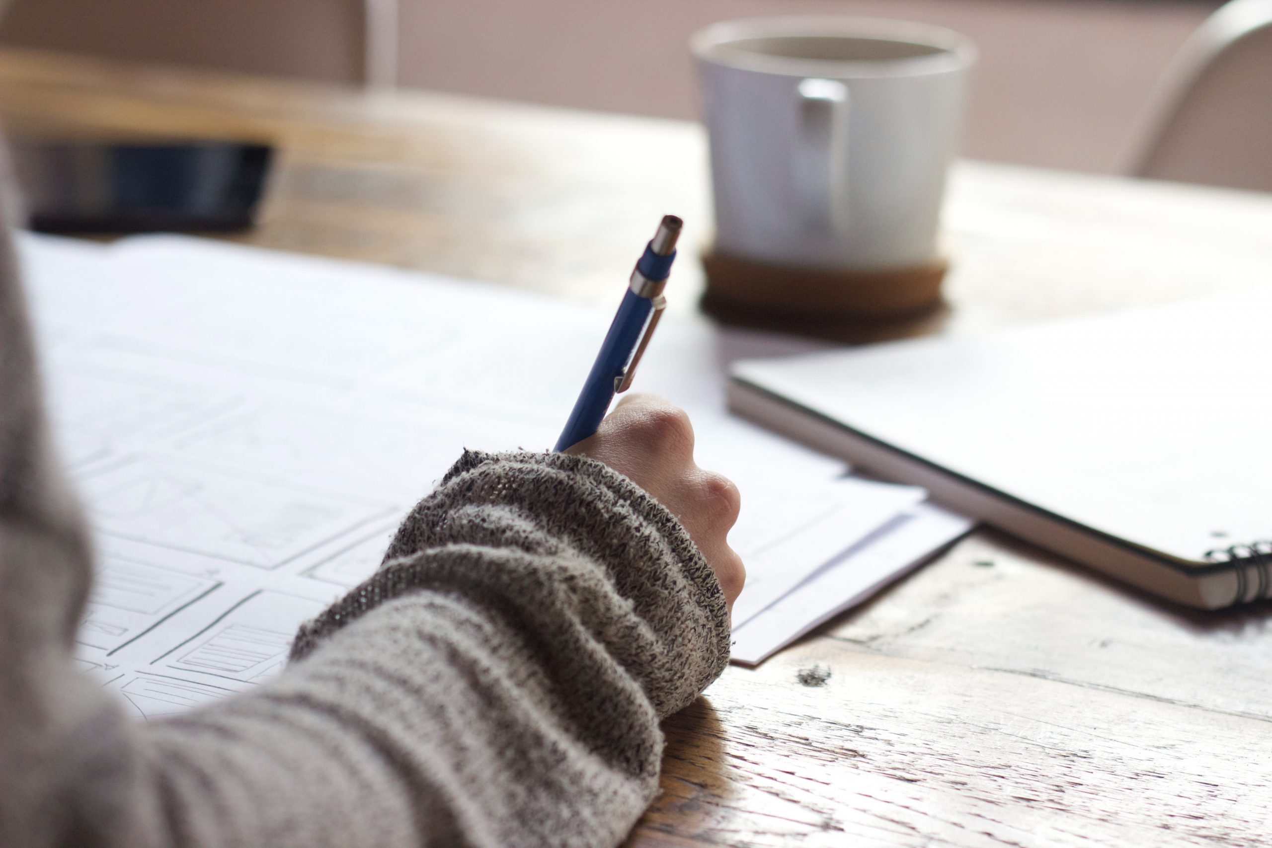 A close up shot of a person writing with a pencil at a workstation.