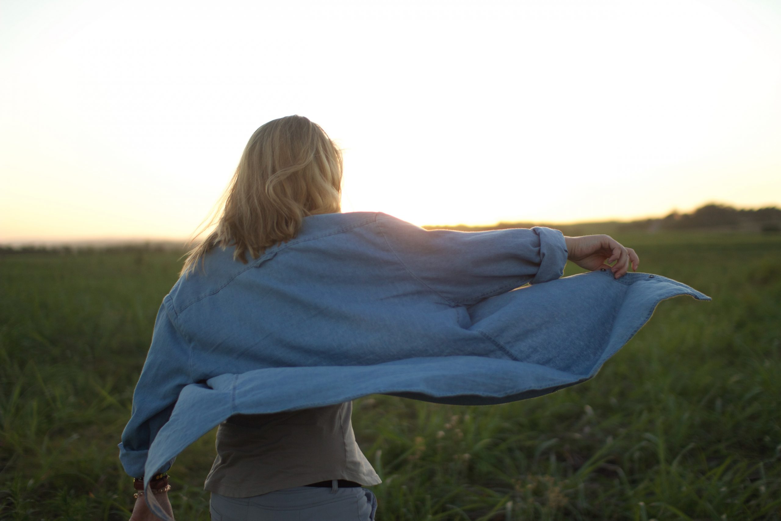 A woman stretches her arm out and holds her jacket as she looks out at the darkening sky.