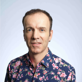 A man with flowers on his shirt smiles directly at the camera