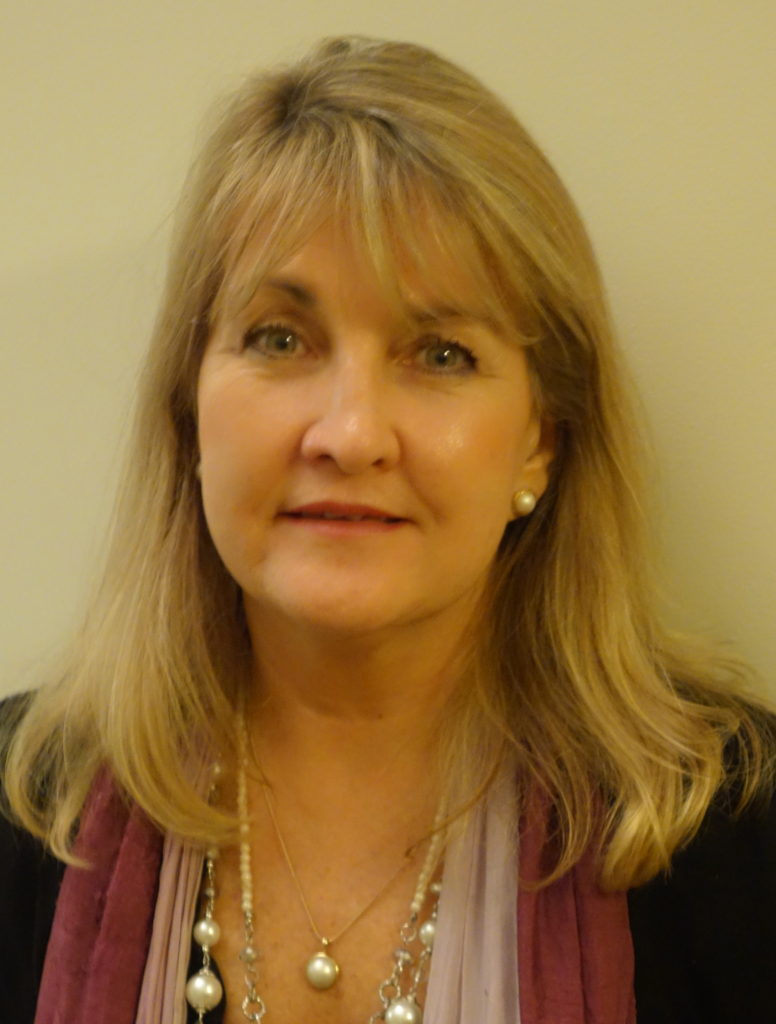 A lady wearing scarves and necklaces smiles at the camera.