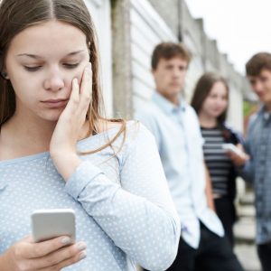 A young woman looks at her phone with concern while others watch.