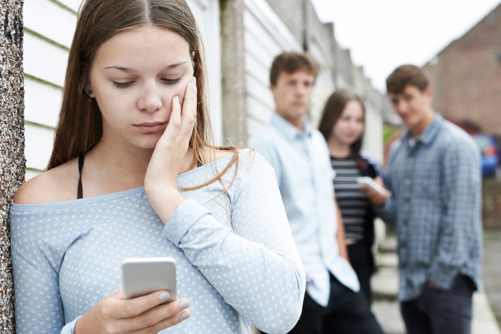 A young woman looks at her phone with concern while others watch.